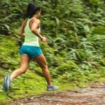 woman in white tank top running on dirt road during daytime